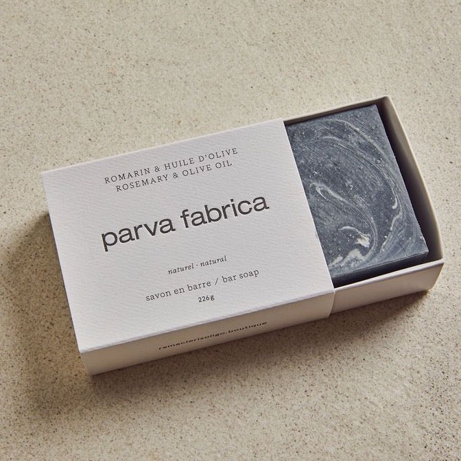 Savon anthracite dans une boîte blanche avec texte, sur fond beige